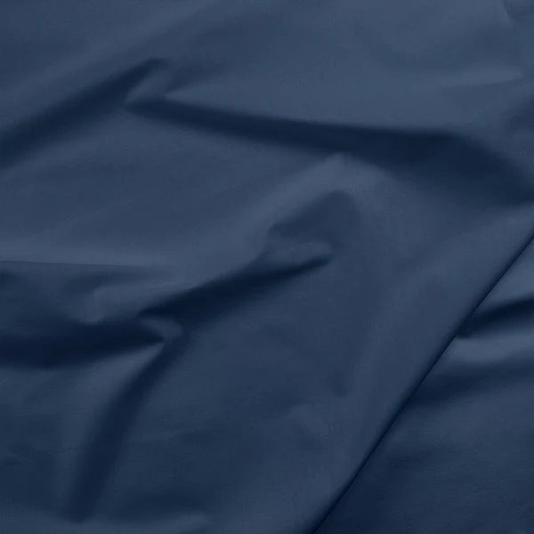 Close-up of Painter's Palette Solids Cadet Fabric Yardage by Paintbrush Studio (PBS), a smooth dark navy blue quilting cotton with gentle folds and natural creases creating subtle shadows and highlights.