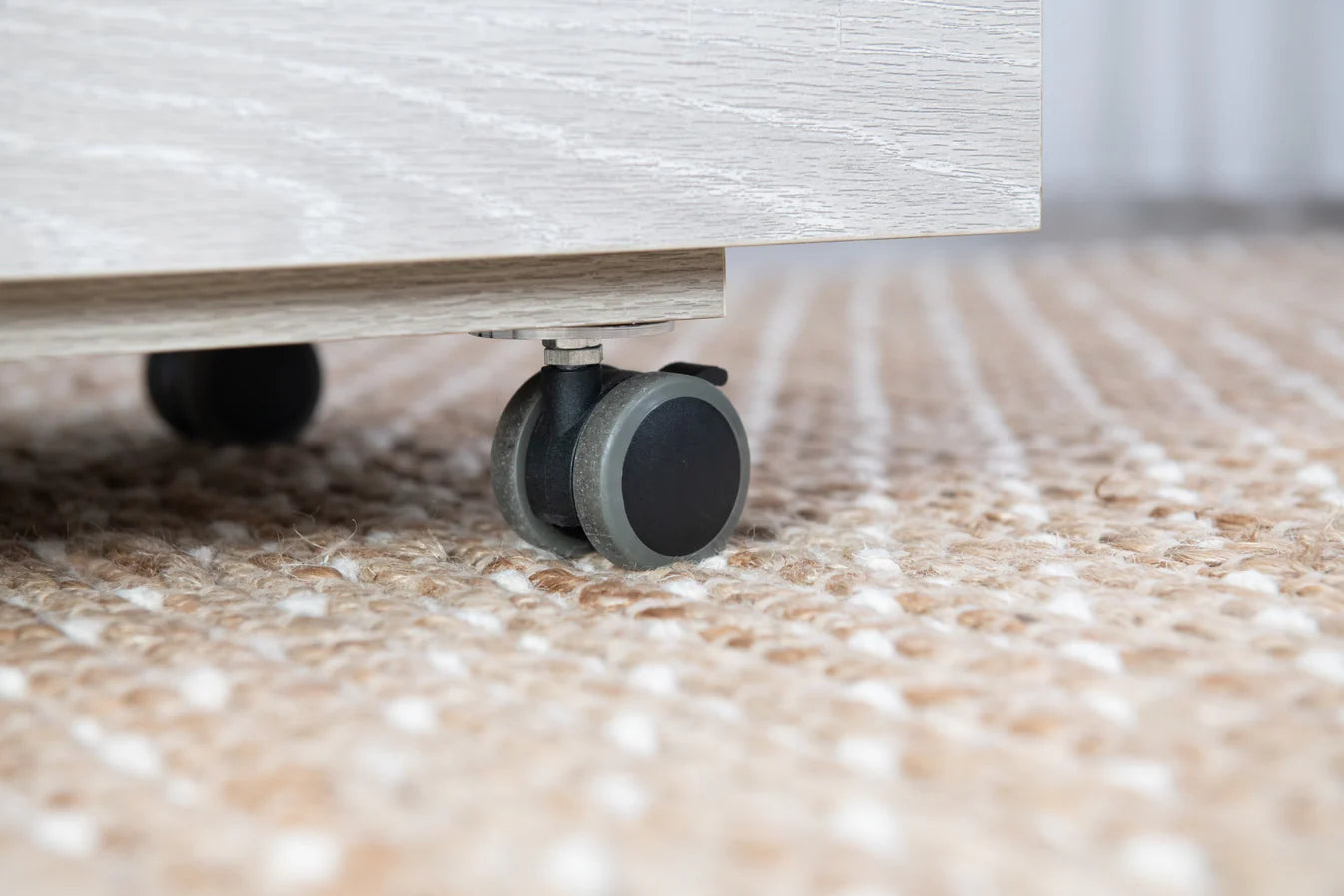 Close-up of a black caster wheel on the Koala Studios Serger Center in White by Koala, shown atop a textured beige carpet, showcasing its mobility and practicality as a serger table or sewing storage solution.