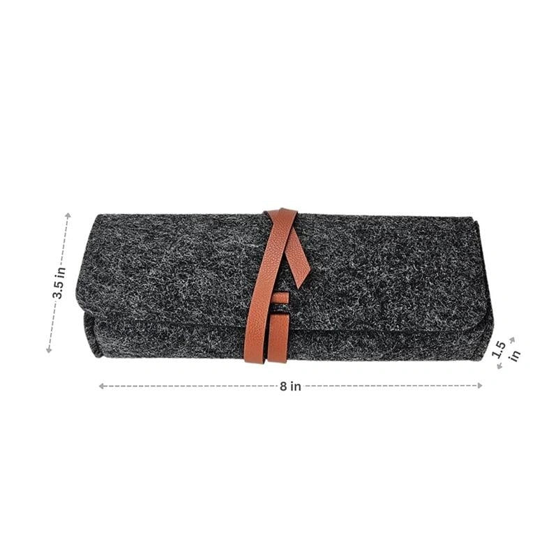 The Felt Pencil Notion Pouch A Grey is a dark gray felt pouch, 3.5" tall, 8" wide, and 1.5" thick, rolled and secured with a brown vegan leather strap—perfect as a stylish craft supplies organizer.