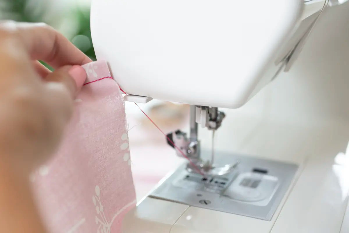 A person guides pink fabric under the needle of a Baby Lock Joy Sewing Machine, preparing to stitch along the edge using its convenient drop-in bobbin.