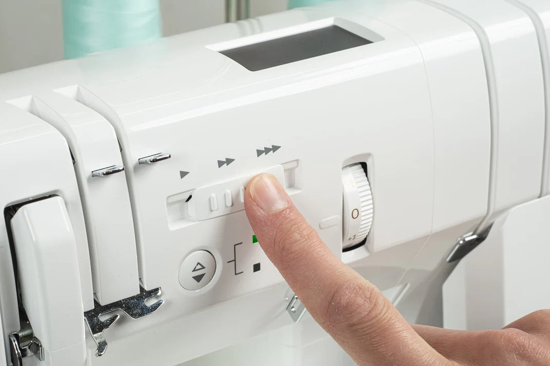 A close-up of a hand adjusting a slider on the white Baby Lock Applaud Deluxe Coverhem Machine, with controls and parts visible—perfect for creating a professional top cover stitch.