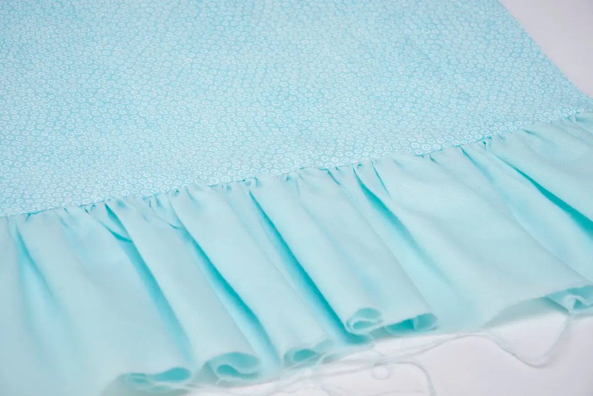Light blue dotted fabric transitions to a gathered, ruffled bottom with unfinished edges and loose threads—ideal for finishing using the Baby Lock Victory Serger Machine and its Jet-Air Threading feature.