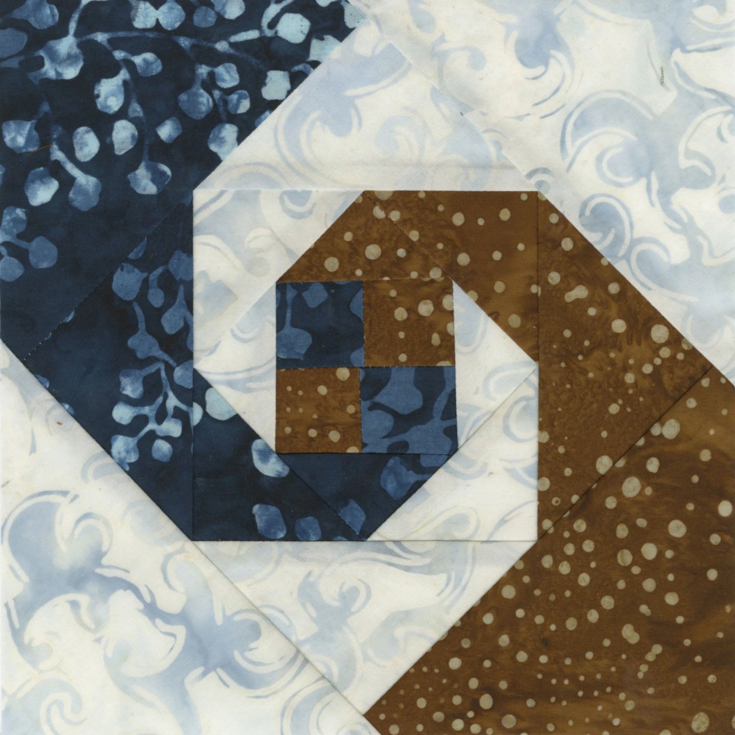 Create precise quilt blocks with spiral designs using blue, brown, and white patterned fabrics by trimming with the Checker Distributor Creative Grids Square on Square Trim Tool for 4in or 8in finished blocks.