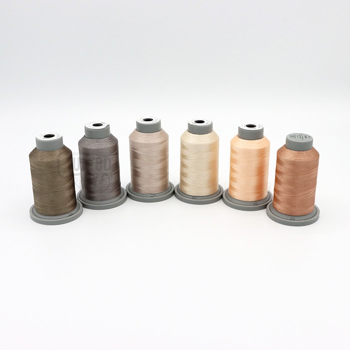 The Hab+Dash Glide Thread New Neutrals Bundle features six spools in beige, brown, and taupe shades, lined up on a white background—perfect for your next Quilted Joy Exclusive project.