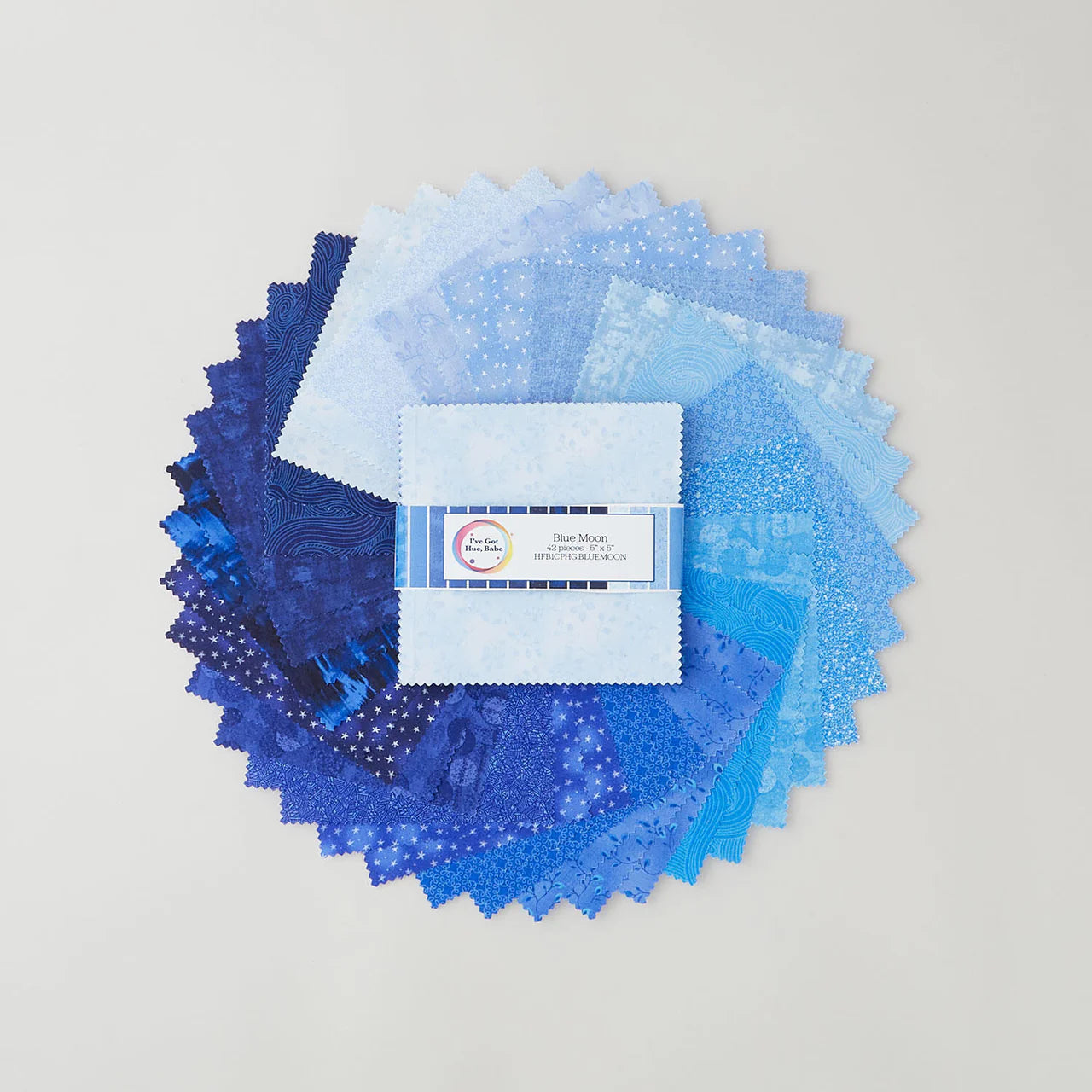 A circular display of Blue Moon fabric swatches in assorted blue hues with stars and dots surrounds a central stack of Jaftex - Henry Glass Fabrics "I've Got Hue, Babe Blue Moon 5" Squares" charm pack with a labeled top.