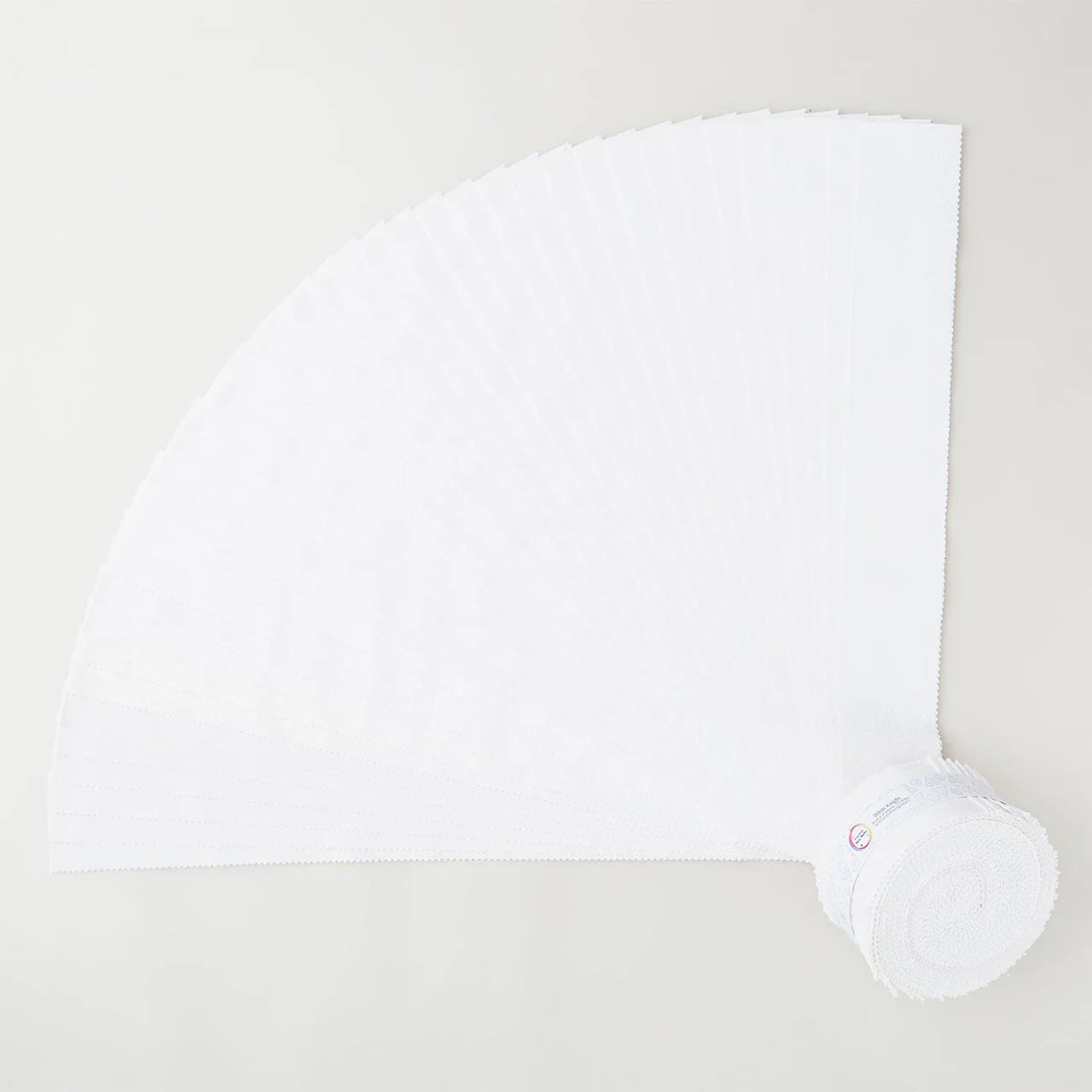 A roll of white disposable napkins is partially unrolled on a light-colored surface, resembling the fan-like pattern of Jaftex - Henry Glass Fabrics I’ve Got Hue, Babe White Knight 2.5in Strips quilt precuts.
