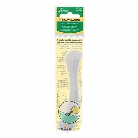 A packaged Hera Marker - Short, a white plastic quilting tool for making fabric creases, is shown in clear plastic packaging with a yellow and green label.