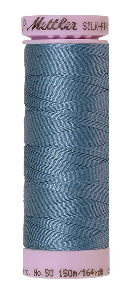 A spool of Mettler Cotton Silk Finish 50wt 150m Laguna thread in light blue with pink plastic ends, labeled as SILK-FINISH COTTON No. 50 150m/164yds—perfect for premium cotton quilting projects.