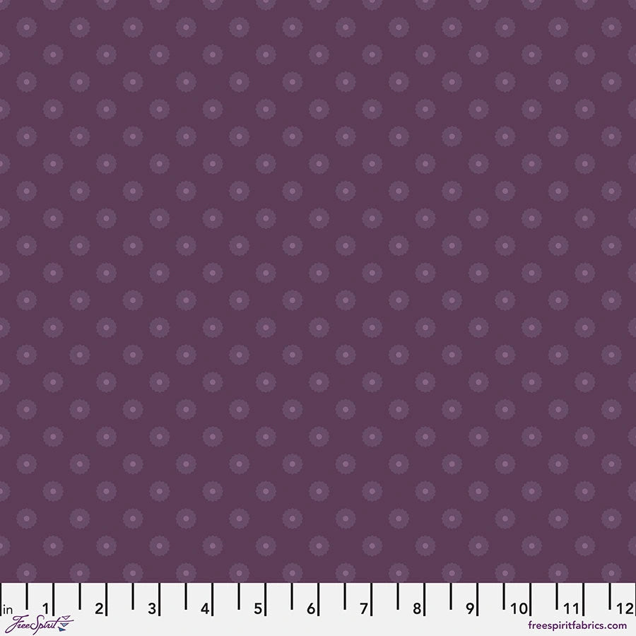 Chromatics Eggplant Blossom Dot Fabric Yardage by Jaftex - FreeSpirit features a dark purple background with lighter purple dot floral motifs. Made from cotton quilting fabric, it includes a white inch ruler (1-12”) at the bottom for scale.