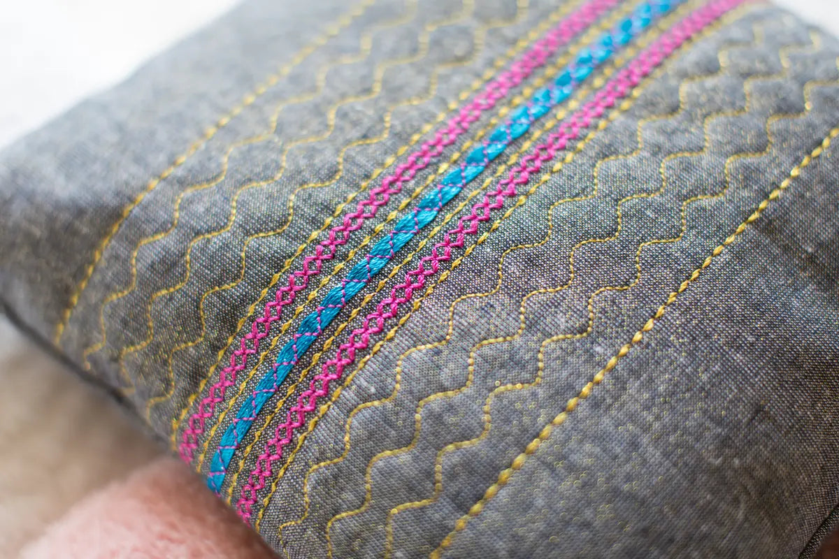 Close-up of gray fabric with decorative stitching—wavy yellow lines and parallel blue and pink stripes—crafted precisely on the Baby Lock Chorus Sewing Machine- FLOOR MODEL.