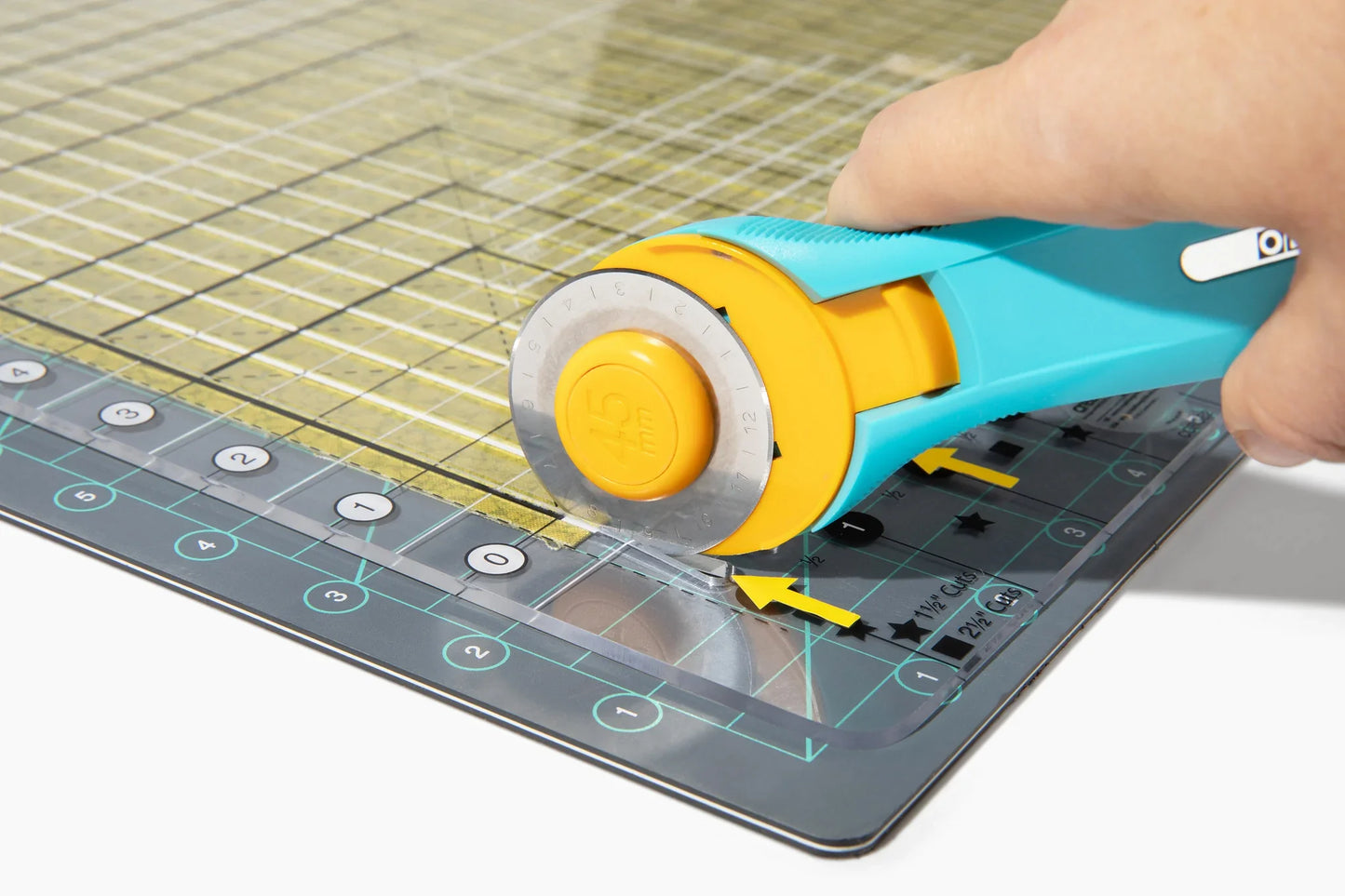 A hand uses a turquoise rotary cutter to cut fabric on a gridded mat, guided by transparent ruler guides and the Quilted Joy Stripology ruler—just like in "Beyond the Strip: Mastering Your Stripology Ruler.