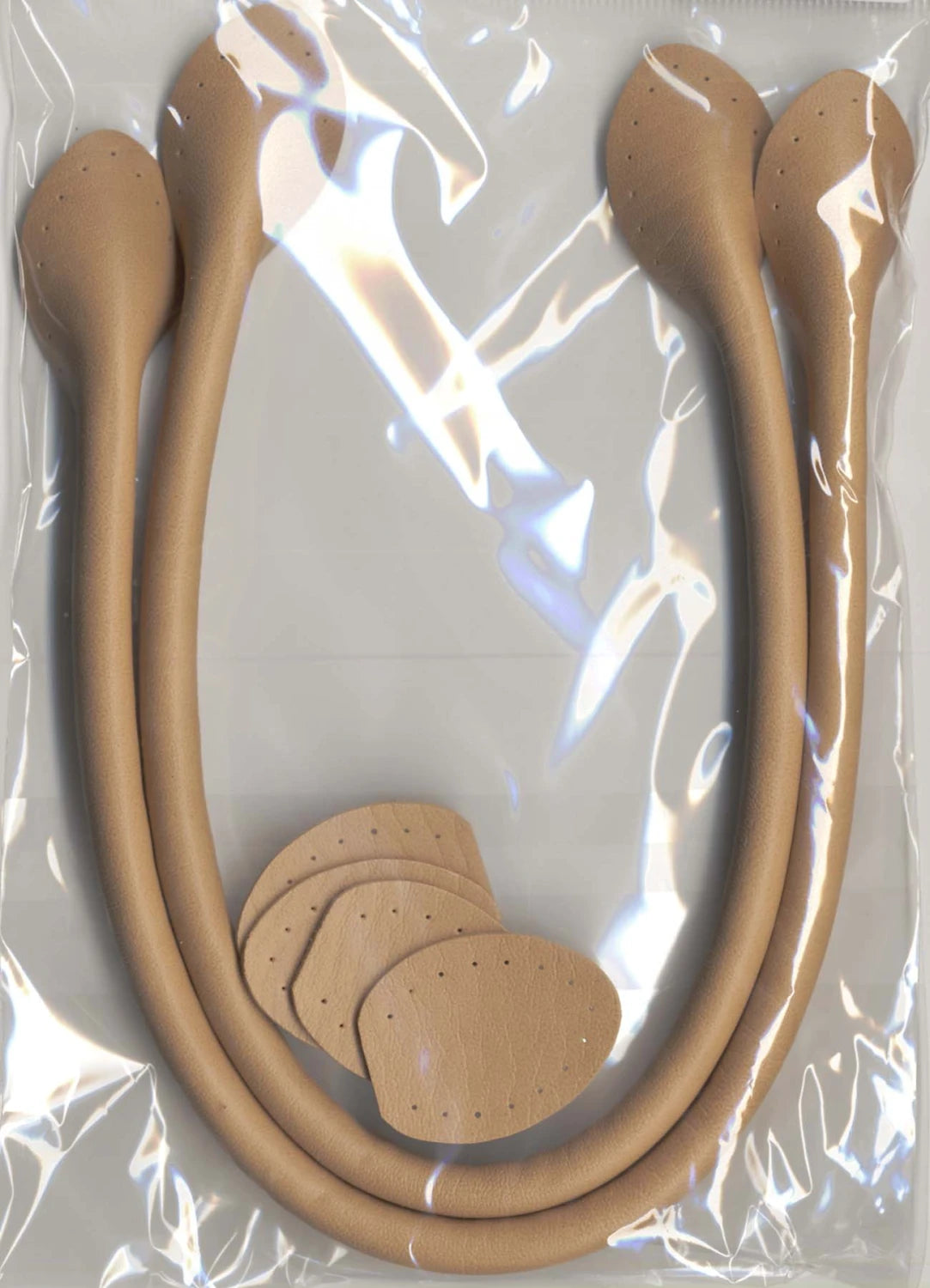 The Checker Distributor Leather Like Bag Handles 20in Beige come with two curved synthetic leather handles and four matching oval patches with holes, all packaged in a clear bag—ideal for DIY bag projects.