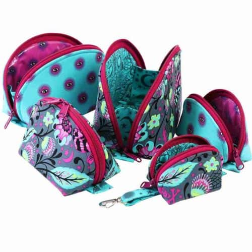 The Clam Up Cases Class by Quilted Joy includes six colorful zippered bags in teal, purple, and floral patterns with bright pink interiors—perfect as cosmetics organizers; some pouches are shown open to display the lining.