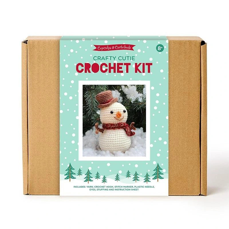 The United Notions Crafty Cutie Snowman Crochet Kit comes in a brown box with a turquoise label showing a crocheted snowman. Ideal for beginners, it includes yarn, needle, eyes, stuffing, and instructions to make your own plushie.