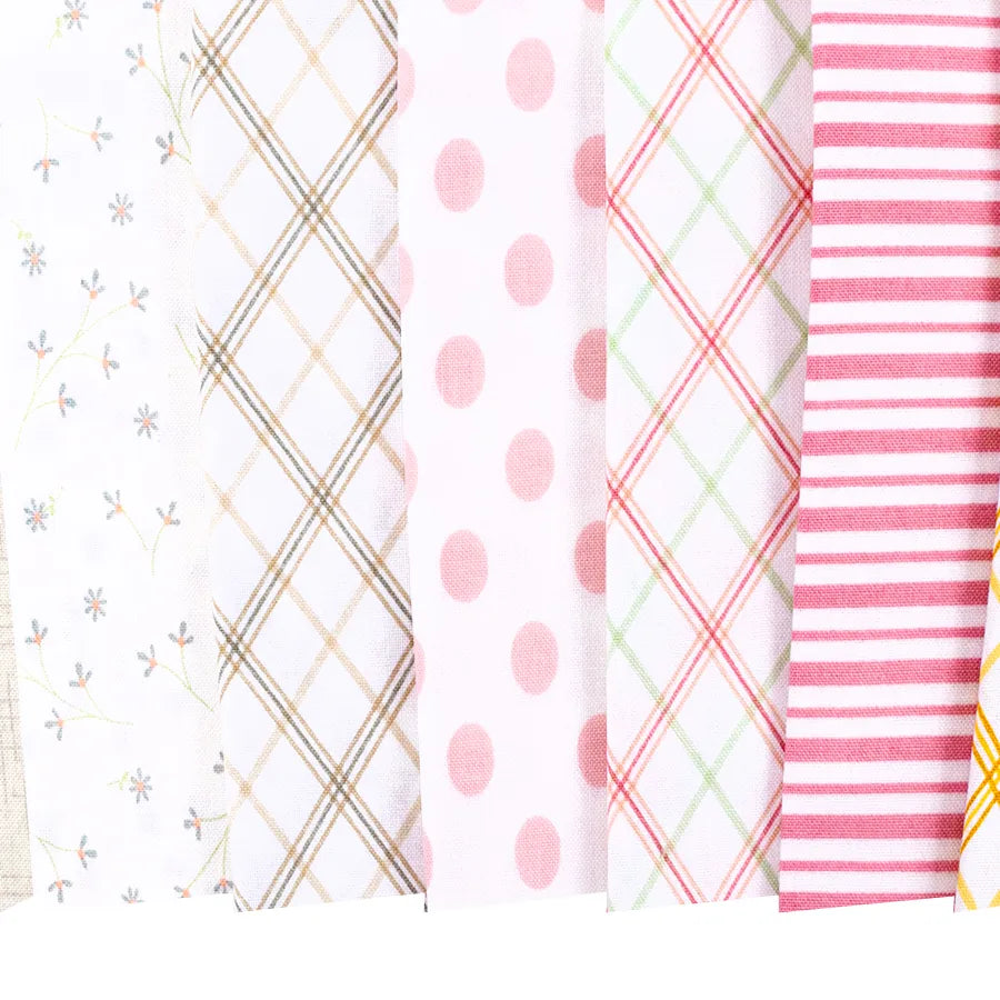 Seven pastel 10" fabric squares from Kimberbell Lullaby are arranged side by side, showcasing patterns like small flowers, plaid, polka dots, and stripes.