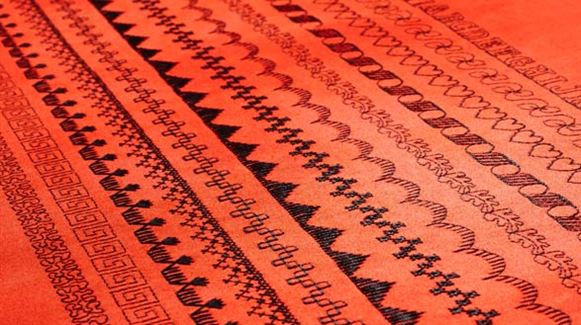 Close-up of red fabric with horizontal rows of black geometric and decorative patterns, such as zigzags and hearts—beautifully stitched with the precision of the SVP Pfaff Passport 2.0 compact sewing machine.