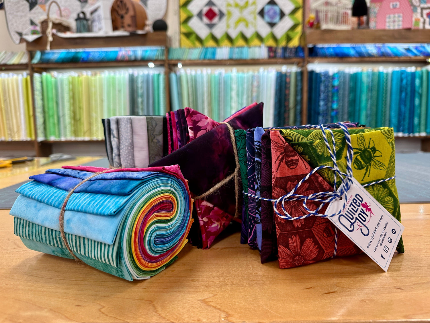 Colorful patterned fabrics with bold floral, fish, and leaf designs in blue, green, purple, and pink hues are arranged in overlapping, vertical and diagonal strips.