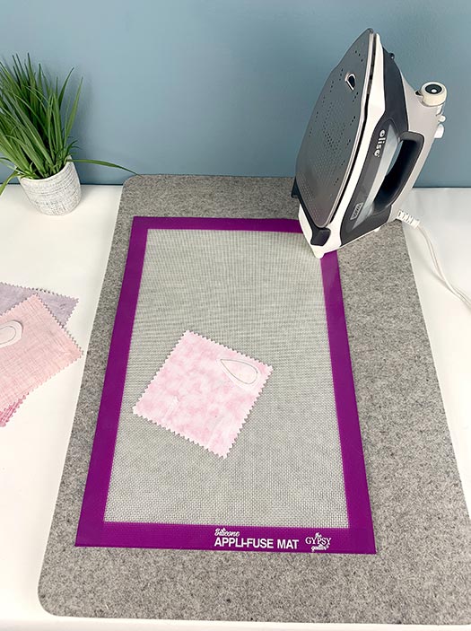 image of a pink square of fabric on a Silicone Appli-Fuse Mat on a wool pressing mat with an iron