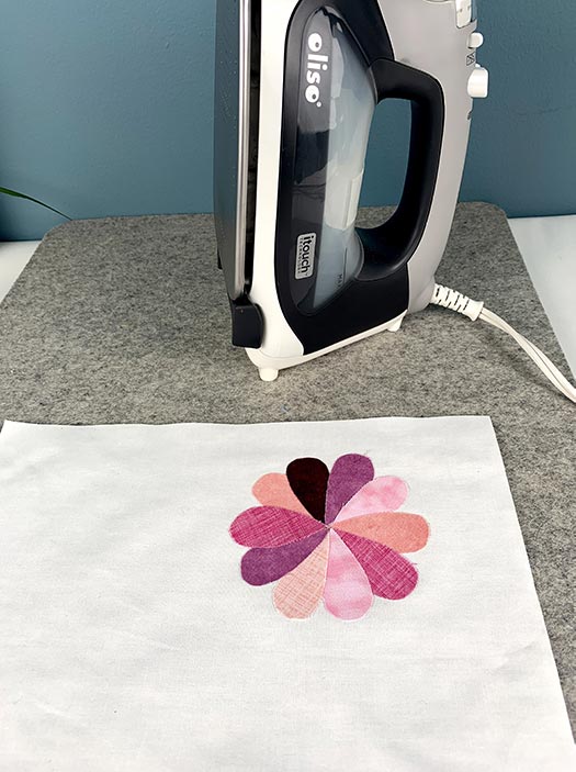 image of applique flower on white fabric with an iron in the background