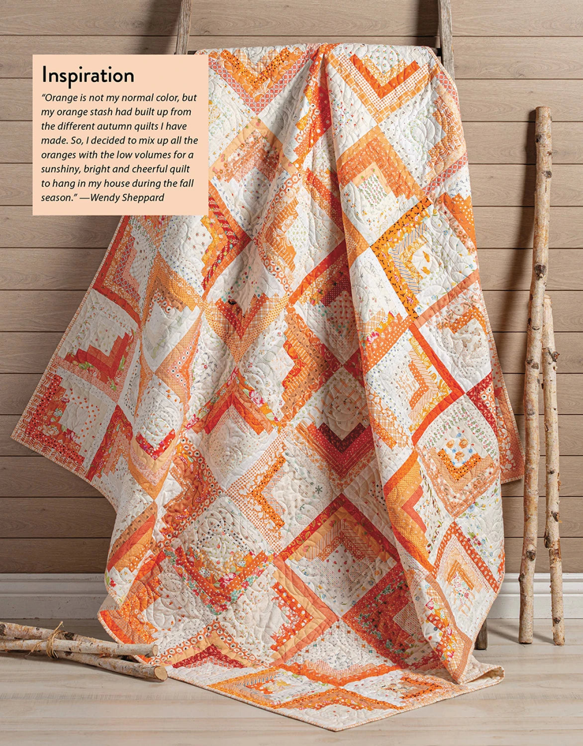 The Checker Distributor’s "Scrap Quilting With Wendy Sheppard" features a vibrant orange, yellow, and cream patchwork quilt draped on a wooden rod beside rustic sticks and wood paneling—autumn quilt inspiration at its best.