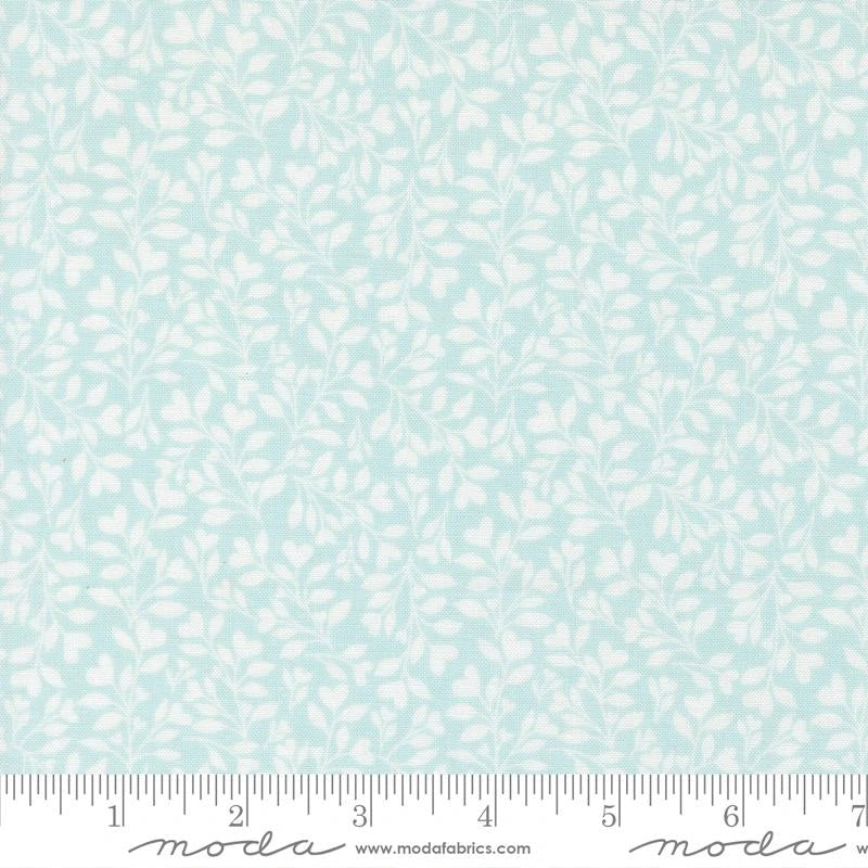 The Abide Light Blue Hearts and Leaves Fabric Yardage by United Notions features delicate white leafy vines on light blue, shown with an inch ruler, making it perfect for baby quilts.