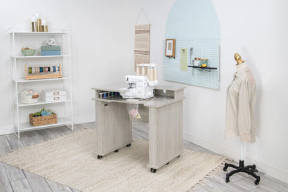 A bright sewing room features the Koala Studios Serger Center in white, holding a serger, shelves with storage for ribbons and supplies, a dress form with a beige shirt, a pegboard for tools, and a woven rug on the light wood floor.