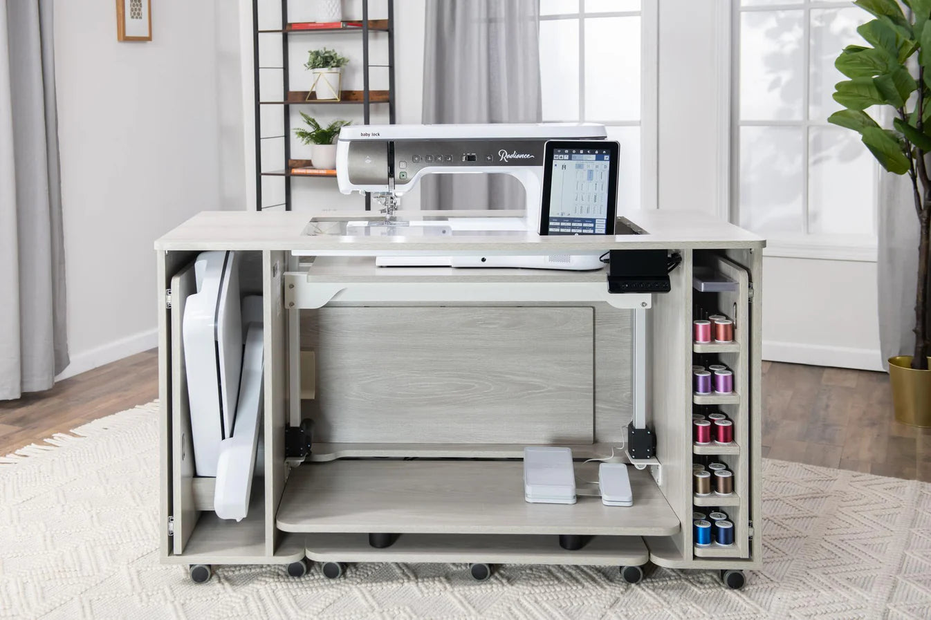 The Koala All-In One Embroidery Studio in White and Gray offers a sleek sewing machine table, open shelves for colorful threads, a folding workspace, and a modern design, perfect for bright rooms with large windows and indoor plants.