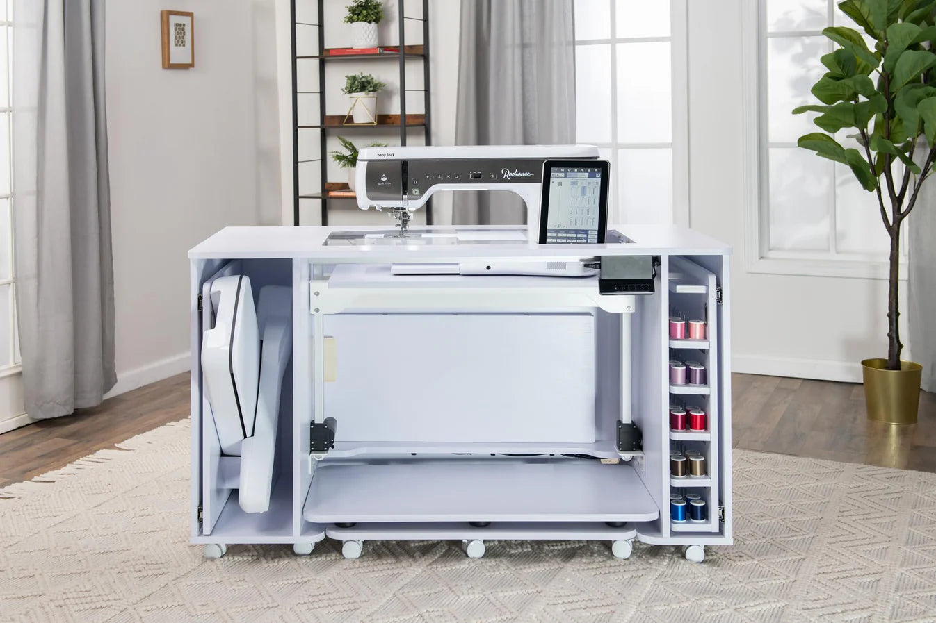 The Koala All-In One Embroidery Studio in White and Gray features a sewing machine, quilting storage shelves for thread spools, a folded ironing board with extra storage below—all set in a bright, stylish room.