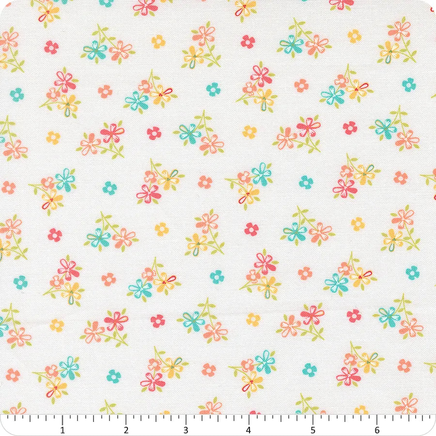 In the Garden Off White Love Me Florals Fabric Yardage by United Notions features a white base with scattered small pink, yellow, green, orange, and blue flowers. A ruler shows scale. Inspired by Corey Yoder's Love Me Florals for Moda.