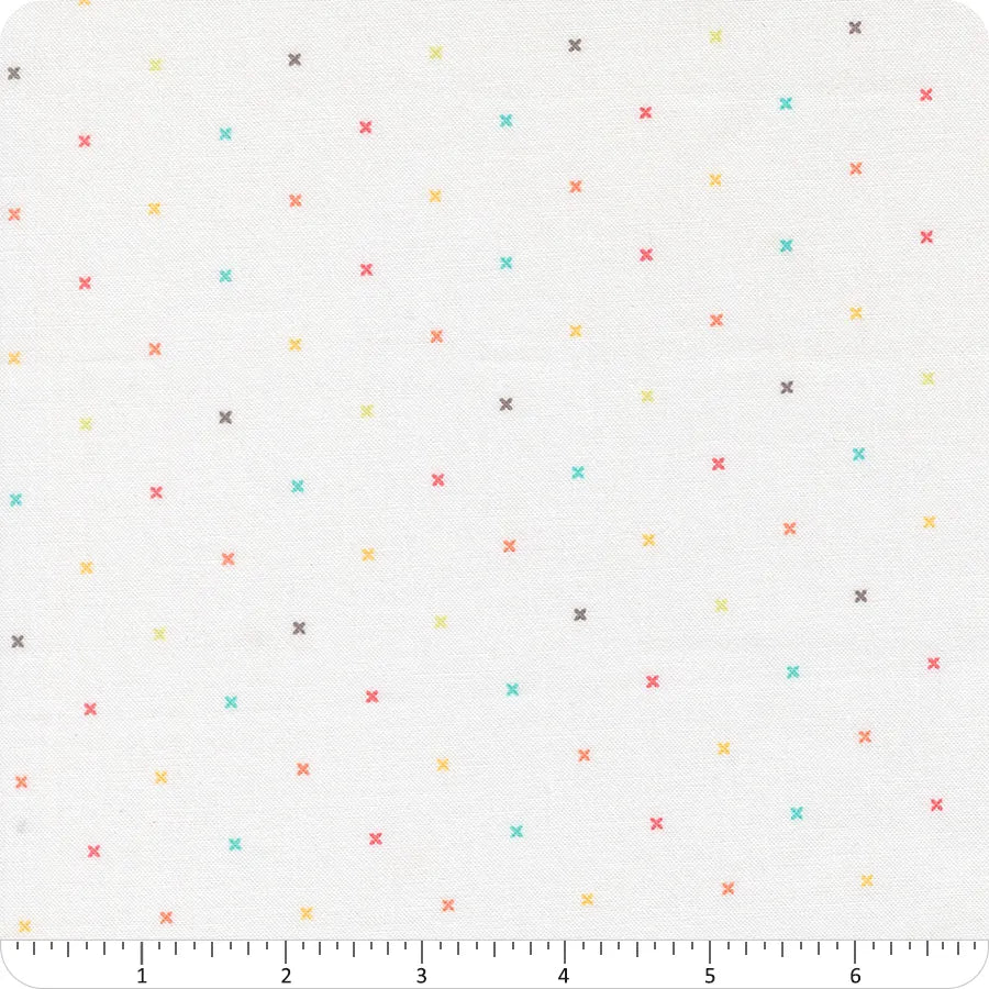 The In the Garden Off White Tiny Peel Fabric Yardage by United Notions features a grid of tiny jeweled X-stitches in red, yellow, aqua, and gray on off white fabric. Includes a ruler along the bottom edge with inch markings from 0 to 6.