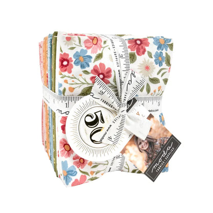 The Wild Honey Fat Quarter Bundle by United Notions features colorful floral quilting fabric squares, neatly stacked and tied with a white measuring tape ribbon, plus a round tag and a card depicting a woman.