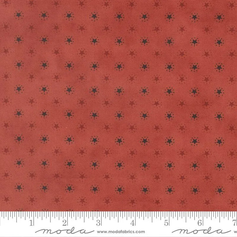 America 250 Years Valor Red Starbright Blenders Fabric Yardage by United Notions features a dusty red fabric with small black starbursts—perfect as a patriotic blender for America 250 Years projects. Ruler at bottom shows inch scale.