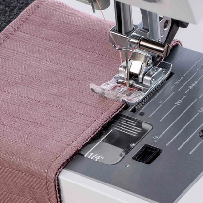 A close-up of a Quilted Joy Pfaff Quilt Ambition 635 Sewing and Quilting Machine stitching pink herringbone fabric, with visible presser foot, needle, and measurement markings—ideal for quilting projects.