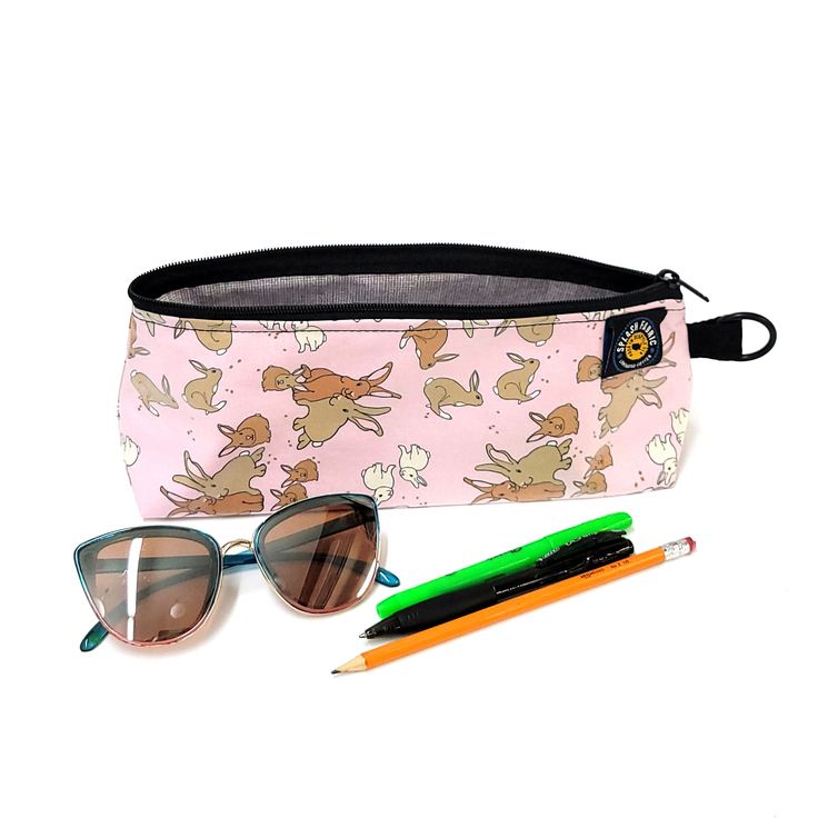 Pencil case with fairy pattern, sunglasses, and pens on a white background