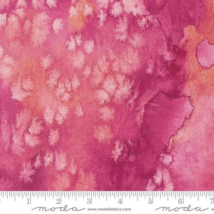 A close-up of United Notions' Soulstice Flow Rose Fabric Yardage displays a pink and orange watercolor pattern with mottled texture; an inch ruler along the bottom edge helps quilters select the perfect cotton yardage.