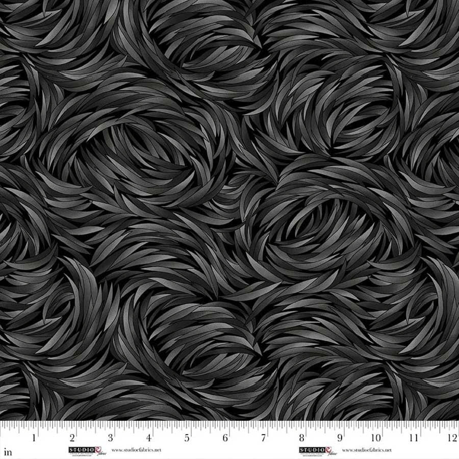 A close-up of QT Fabrics' Tempest Charcoal Swirl 108" Wide Quilt Backing Fabric shows a black and dark gray feather or leaf pattern, with a ruler along the bottom edge marking inches 1–13 to illustrate the fabric's scale.