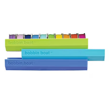 The Checker Distributor Bobbin Boat is a set of three colorful plastic sewing organizers—green, teal, and blue—designed to neatly hold multiple sewing bobbins with assorted threads for compact storage.