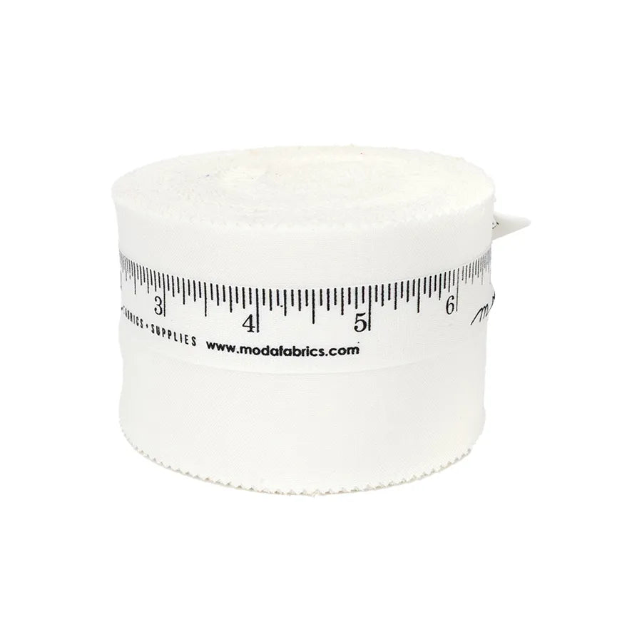 A rolled strip of Bella Solids Off White Junior Jelly Roll by United Notions, with a black ruler design and modafabrics.com on the side, is displayed against a plain white background.