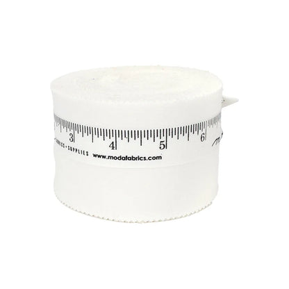 A rolled strip of Bella Solids Off White Junior Jelly Roll by United Notions, with a black ruler design and modafabrics.com on the side, is displayed against a plain white background.