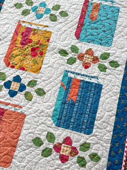 The Novel Idea Quilt Pattern by Riley Blake features jars in vibrant fabrics with green leaf accents on a white polka dot background—perfect for fans of Little Women quilt designs and Orchard House fabric.