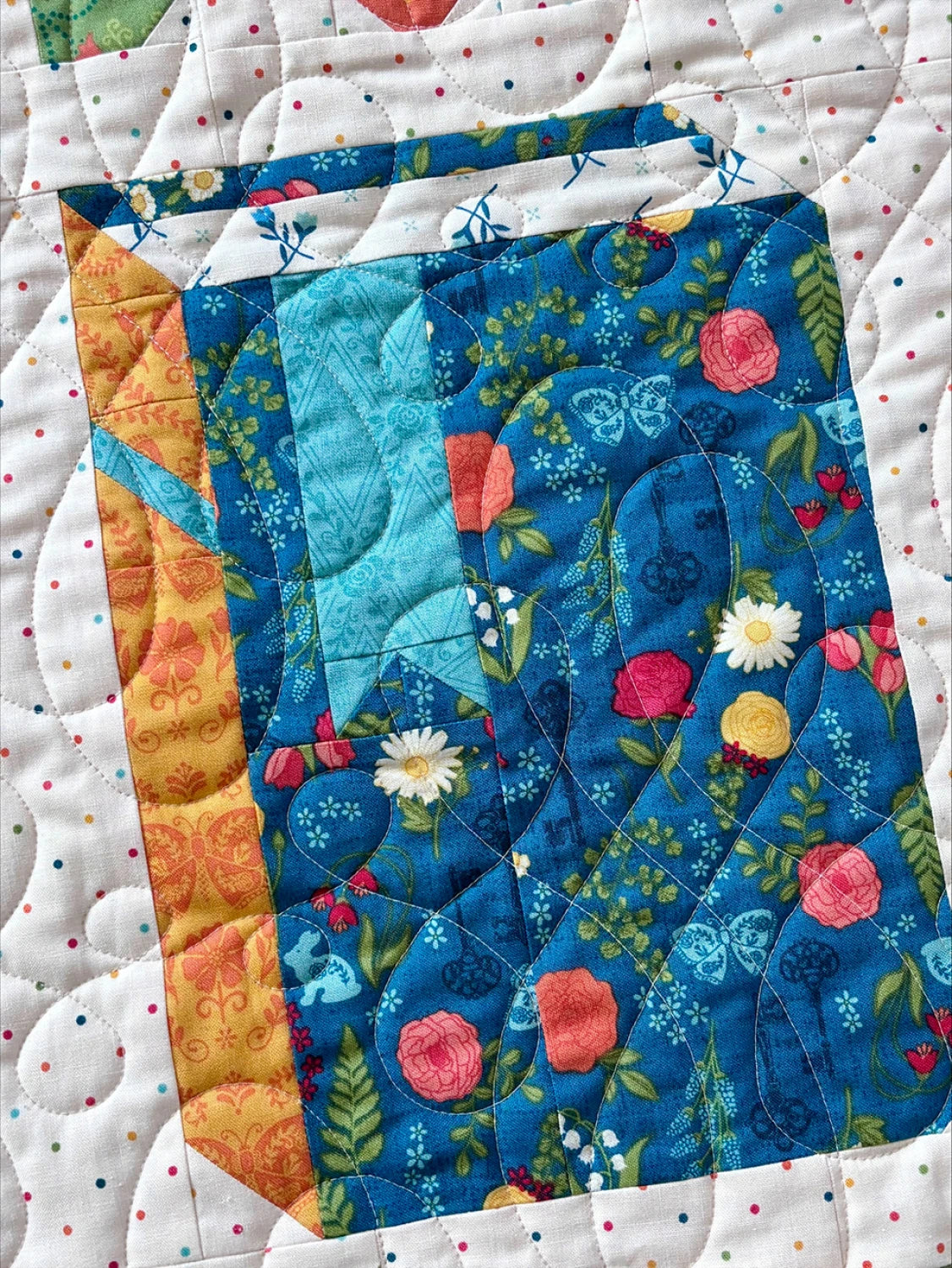 The Riley Blake "Novel Idea Quilt Pattern" features a carton-shaped block with floral and geometric fabrics in blue, yellow, and orange on a white background with multicolored dots—perfect for book lovers.