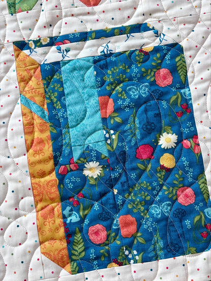 The Riley Blake "Novel Idea Quilt Pattern" features a carton-shaped block with floral and geometric fabrics in blue, yellow, and orange on a white background with multicolored dots—perfect for book lovers.