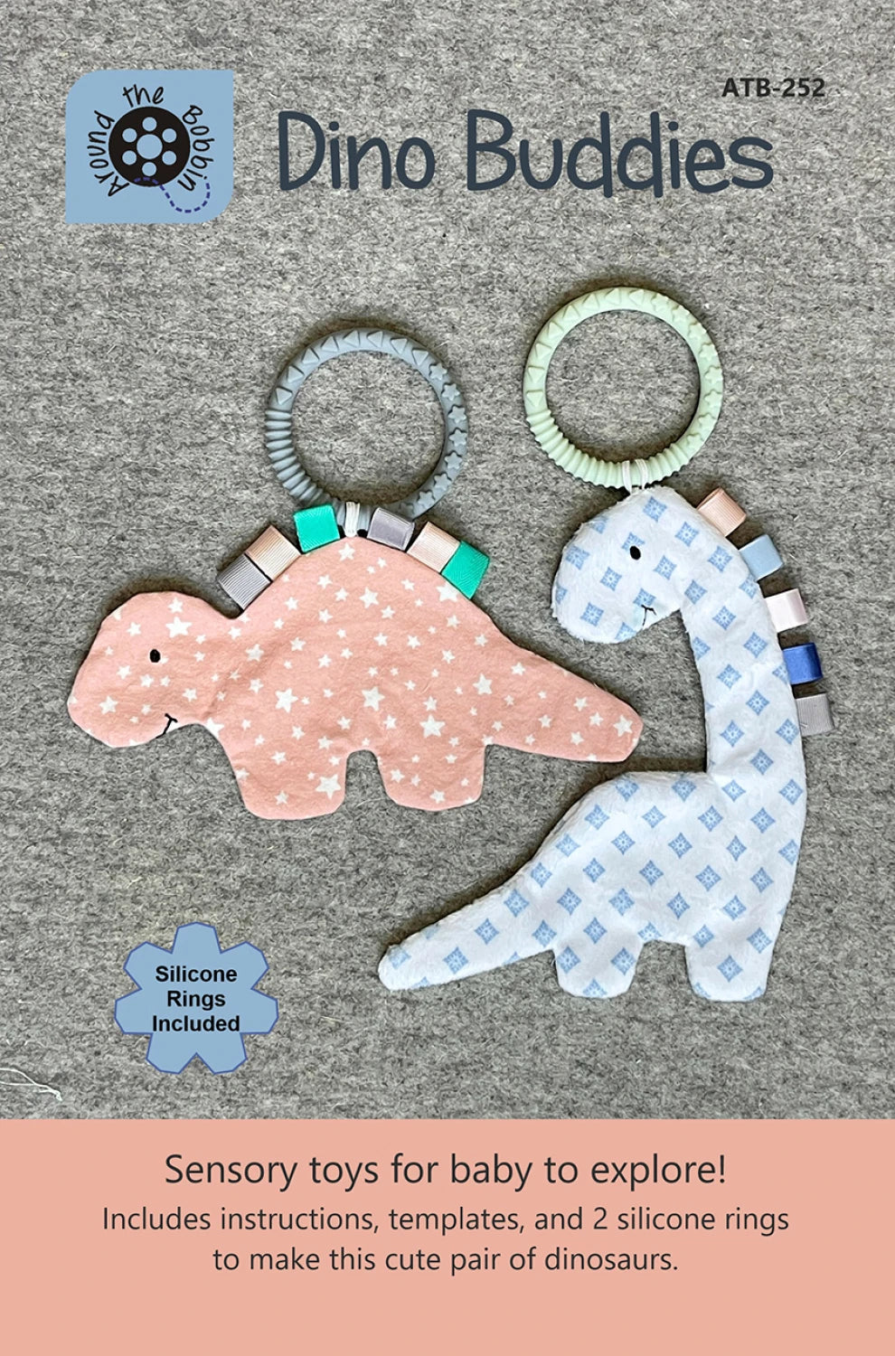 Two soft dinosaur toys, one pink and one blue, with baby-safe silicone rings, rest on a gray background. Above them is "Dino Buddies Pattern" by Checker Distributor, with sensory toy details for babies shown below.