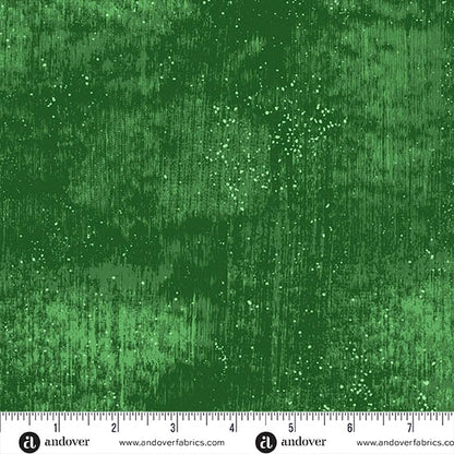 A close-up of Andover’s Glaze Juniper 108" Wide 3 Yard Quilt Fabric Back Pack shows green textured fabric with a mottled, streaky look and white speckles. A ruler displays inches 0–7—perfect for extra wide quilt backing.