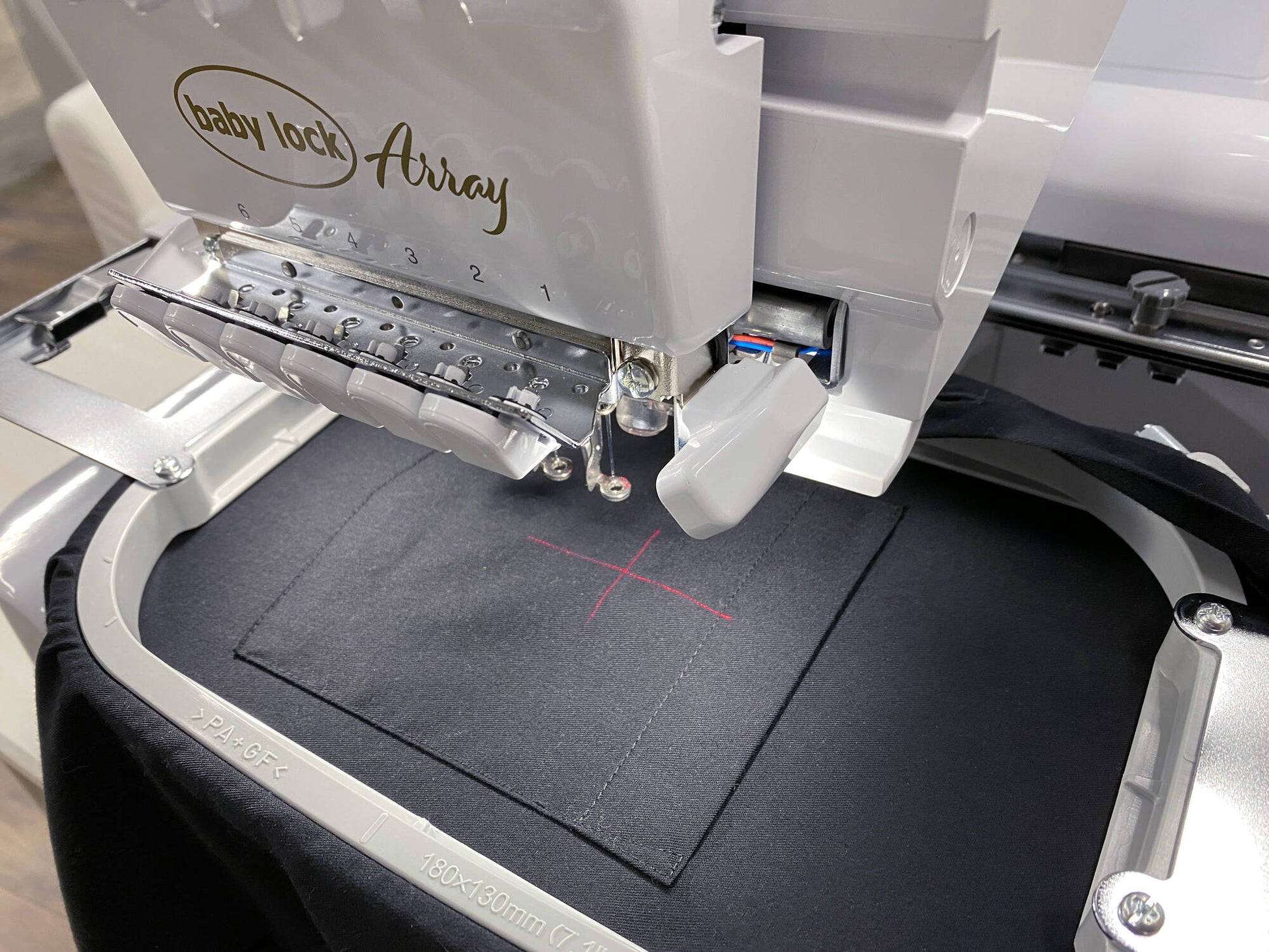 A close-up of the Baby Lock Array 6 Needle Embroidery Machine stitching a red cross on black fabric held in an embroidery hoop.