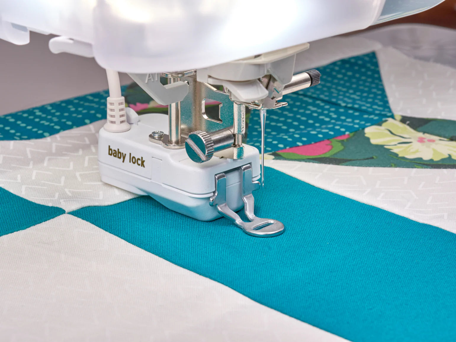 Close-up of the Baby Lock Anthem Sewing & Quilting Machine with FREE 60 Days of Online Classes, quilting teal and white geometric patterns and a floral section, featuring StitchSync Regulation with the presser foot and needle in action.