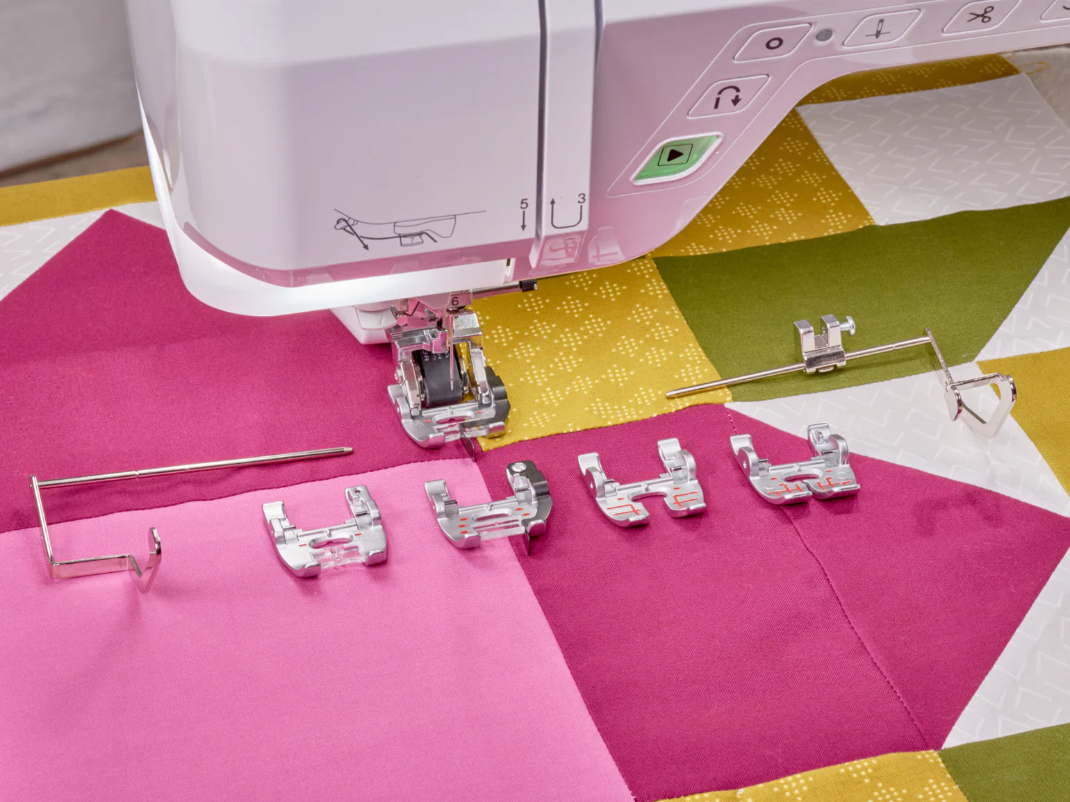 A close-up of the Baby Lock Anthem Sewing & Quilting Machine with six presser feet on a colorful pink, yellow, and green patchwork quilt—includes FREE 60 days of online classes for enhanced StitchSync Regulation.