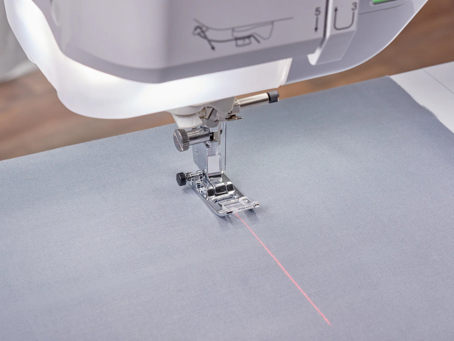 A close-up of the Baby Lock Anthem Sewing & Quilting Machine with FREE 60 Days of Online Classes shows its presser foot and needle over gray fabric, highlighting the red laser guideline for precise stitching and StitchSync Regulation.