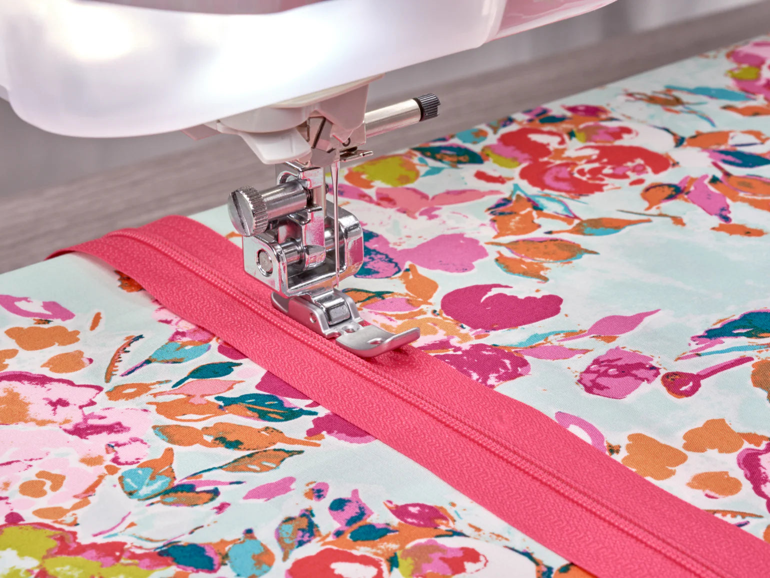 The Baby Lock Anthem Sewing & Quilting Machine with FREE 60 Days of Online Classes stitches a bright pink zipper onto floral fabric. Its StitchSync Regulation keeps the needle close to the edge, securing the zipper with precision.