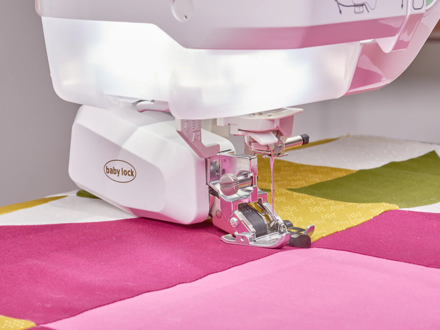 A close-up of the Baby Lock Anthem Sewing & Quilting Machine with FREE 60 Days of Online Classes, featuring StitchSync Regulation as it stitches vibrant pink, green, and yellow fabrics from a colorful quilting bundle.